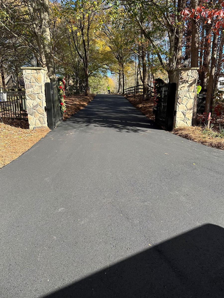 Long freshly paved driveway through a stone gate