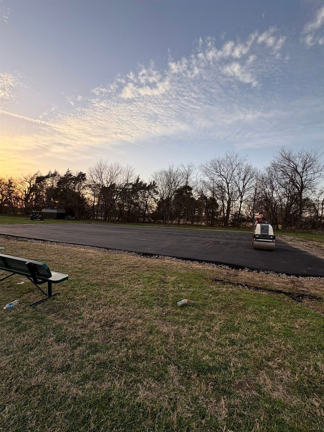 ECA crew member rolling a fresh asphalt pad at sundown